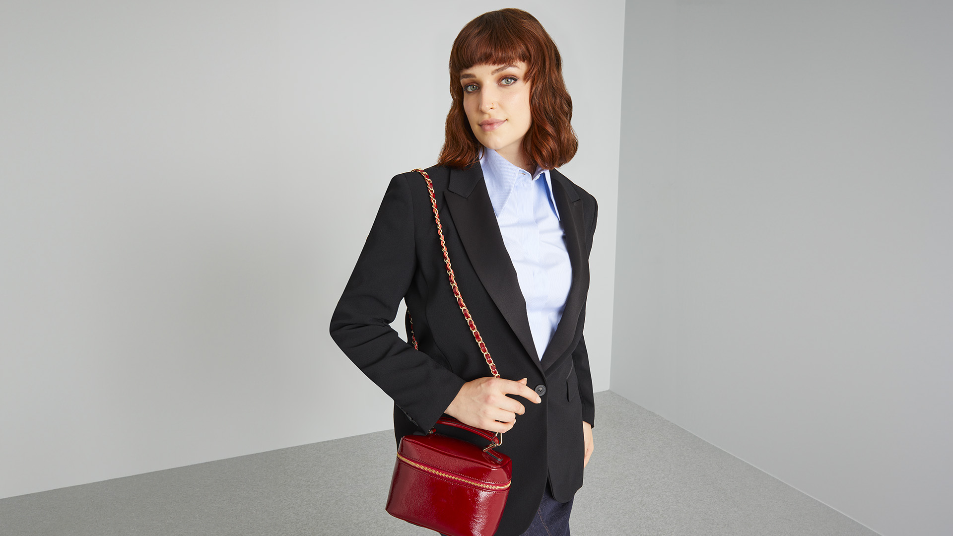 Modella indossa giacca nera con camicia azzurra e borsa bordeaux.